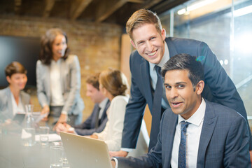 Businessmen smiling at laptop in conference room meeting