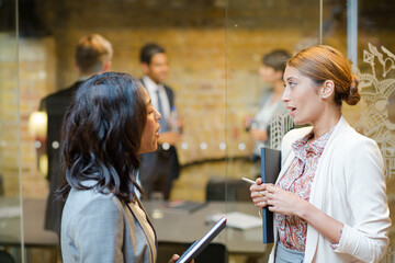 Businesswomen talking outside conference room meeting