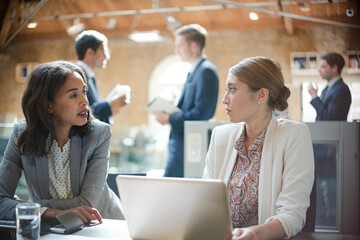 Businesswomen talking and working at laptop in office