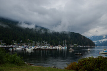 Fototapeta na wymiar Sail, yachts and motor boats anchor in the harbor. Calm water and the green misty mountains after rain. Deep Cove, British Columbia, Canada