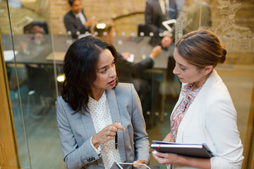 Businesswomen talking outside conference room meeting