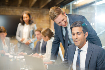 Businessmen smiling at laptop in conference room meeting