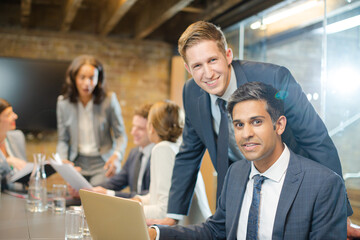 Businessmen smiling at laptop in conference room meeting