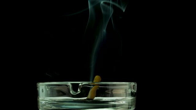A cigar is smoldering in an ashtray against a black background of copy space. Cigarette smoke