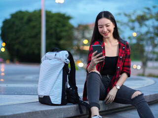 Confident female tourist backpacker sitting on stairs and using smartphone