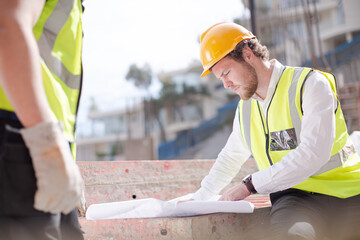 Construction worker engineer reviewing blueprints at highrise construction site