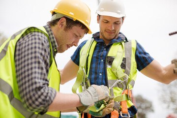 Construction worker fastening coworker‚Äö√Ñ√¥s safety harness