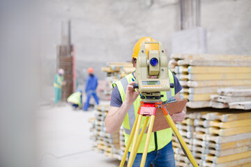 Engineer with clipboard using theodolite at construction site