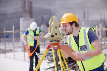 Engineer with clipboard using theodolite at construction site