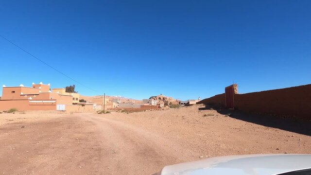 Vehicle Driving On Dirt Road Through Clay Brick Buildings Under Clear Blue Sky In Tinghir, Morocco. POV
