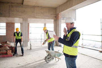 Foreman with digital tablet using walkie-talkie at construction site