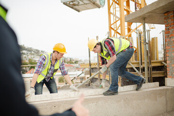 Fototapeta na wymiar Construction workers using level tool below crane at construction site