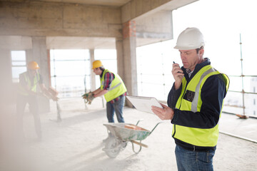 Foreman with digital tablet using walkie-talkie at construction site