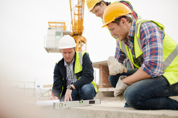 Construction workers using level tool below crane at construction site