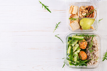 Lunch box filled with oatmeal, cucumber salad, and nuts, bread, pear on white wooden background....