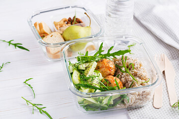 Lunch box filled with oatmeal, cucumber salad, and nuts, bread, pear on white wooden background. Lunchbox dinner.