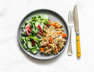 Delicious healthy lunch - bulgur pilaf with chicken breast and fresh vegetable salad on a light background, top view