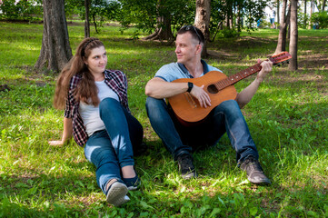 Young couple on the grass in the park in the summer, a guy plays the guitar for a girl