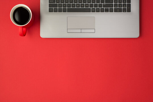 Top view photo of laptop and red cup of coffee on isolated red background with empty space