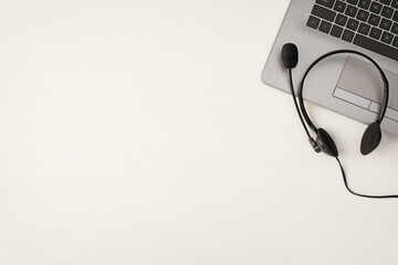 Top view photo of wired headphones with microphone on laptop on isolated white wooden table...