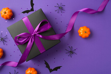 Top view photo of halloween decorations small pumpkins bats spiders black giftbox with purple ribbon bow and confetti on isolated violet background with blank space