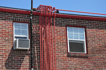 Red brick building with red pipes and one open window and one with air conditioner unit