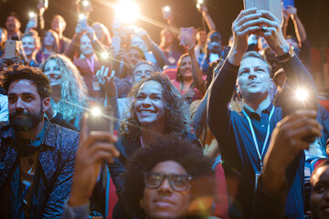 Eager audience with smart phone flashlights in dark auditorium