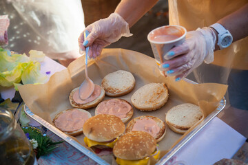 A man spreads sauce on burger buns.