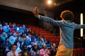 Audience watching male speaker with arms outstretched on stage