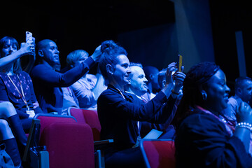 Fototapeta na wymiar Audience members with smart phones videoing speaker on stage at conference