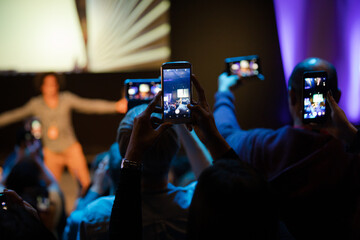 Audience members with smart phones videoing speaker on stage at conference