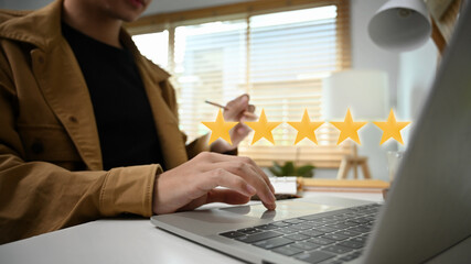 Man hand pressing on laptop computer giving positive feedback with gold five star rating.
