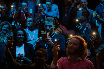 Fototapeta premium Smiling audience using smart phone flashlights for speaker