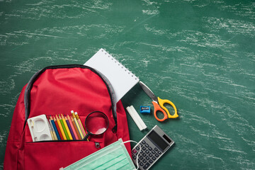 Top view of stylish red school bag backpack at a green blackboard with face mask protection and...
