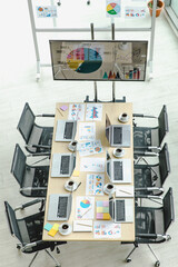 Top view shot of conference meeting room in company office full of laptop notebook computers on working desk with black chairs and big screen monitor and glass board with post it data paper documents