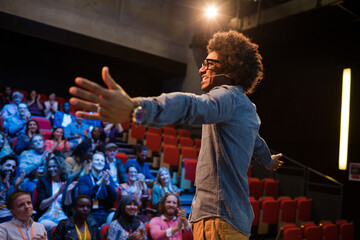 Audience watching male speaker with arms outstretched on stage