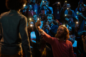 Fototapeta na wymiar Smiling audience using smart phone flashlights for speaker