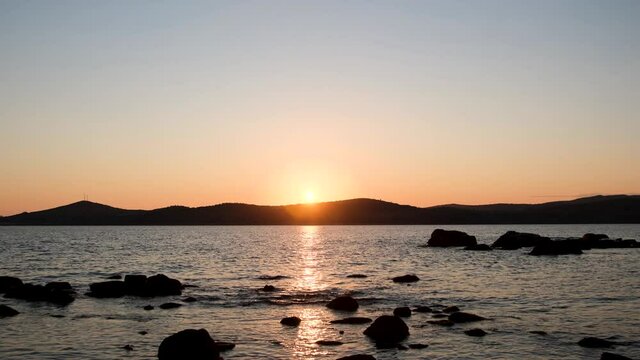 a warm summer evening sunset on the shore of the mora through the strait, the sun almost went down behind the mountains, there are many stones on the near shore