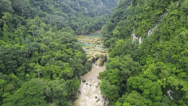 Drone aerial footage of Guatemalan rainforest Semuc Champey National Park and river Rio Cahabon surrounded by bright green rainforest hillsides and mountains. Camera tracking forwards. 