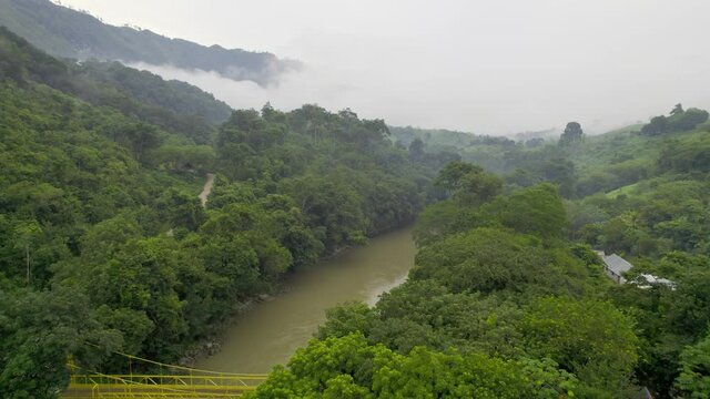 Drone aerial footage of river Rio Cahabon near Semuc Champey National Park in Guatemala surrounded by bright green rainforest trees on a cloudy day near Chicanutz. Camera tracking left.