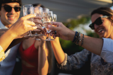 Group of happy friends drinking and toasting champagne outdoors in the terrace - Friendship concept with young people having fun together celebrating in the garden