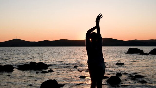 warm summer evening sunset on the shore of the mora through the strait, there are many stones on the near shore and the girl stands with her back and throws stones into the water