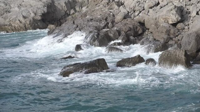 Water splashing. Water beats against seashore. Sea waves of blue water beat against the coastal rocks. Sea waves of blue-gray water beat against the coastal rocks. Novy Svet. Crimea.