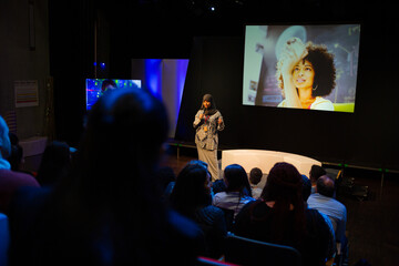 Smiling female speaker in hijab talking with microphone on stage