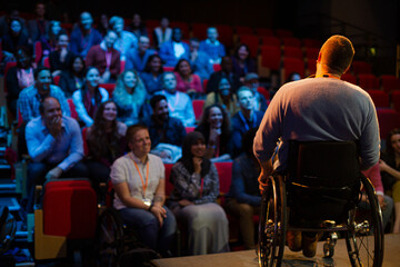 Fototapeta na wymiar Speaker in wheelchair on stage talking to conference audience