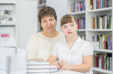 Portrait of a senior woman and girl with syndrome down at library. Education for disabled children concept