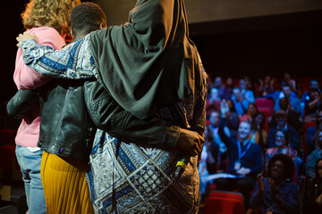 Speakers hugging on stage for audience at conference