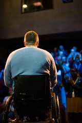 Speaker in wheelchair on stage talking to conference audience