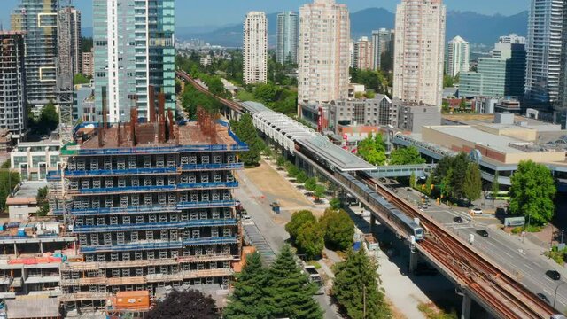 SkyTrain Transit Leaving At Metrotown Station With City Traffic In Burnaby, BC, Canada. - aerial pullback
