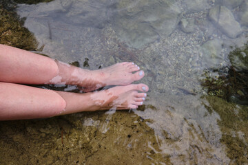 feet of an unrecognizable woman stuck in the cold water of a mountain river to improve the circulation of the blood. cardiovascular health,
